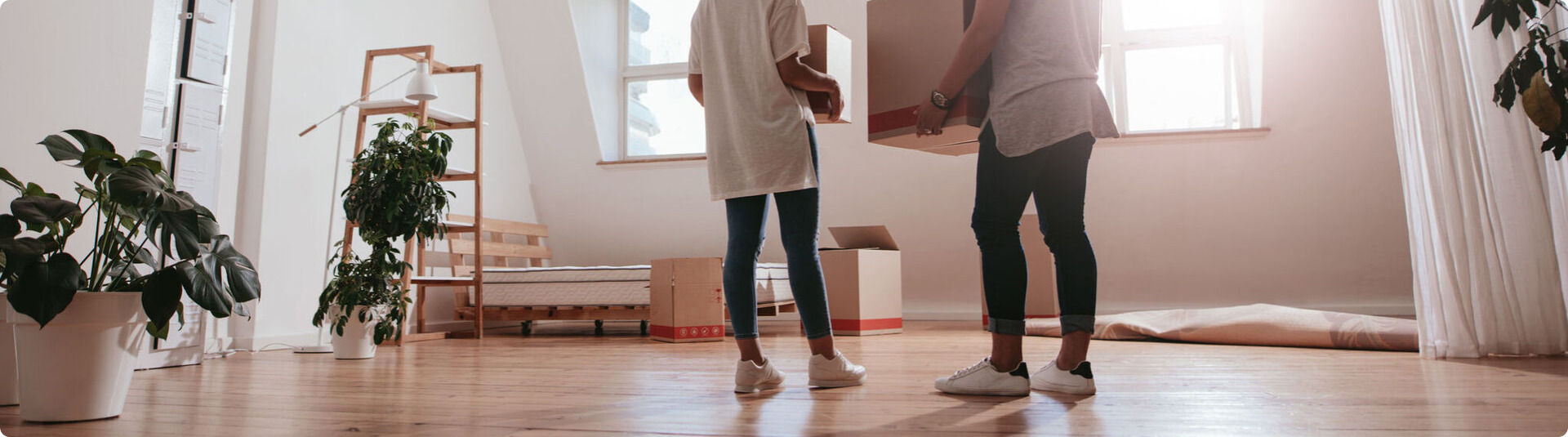 Full length rear view shot of young couple carrying cardboard box at new home. Young man and woman holding boxes and moving in new house.