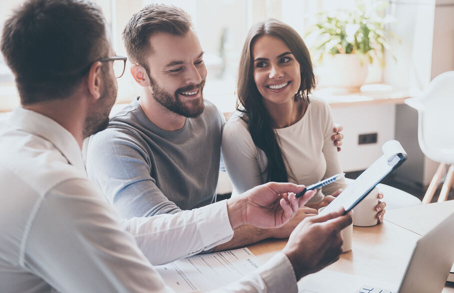 Three people having a meeting while someone points at a clipboard with a pen