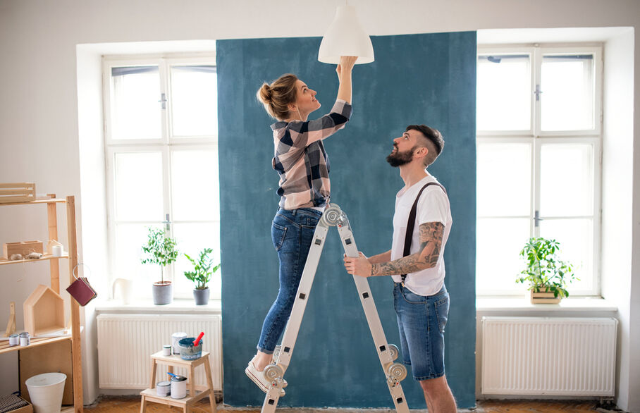 Someone holding a ladder which someone is climbing and fitting a light bulb
