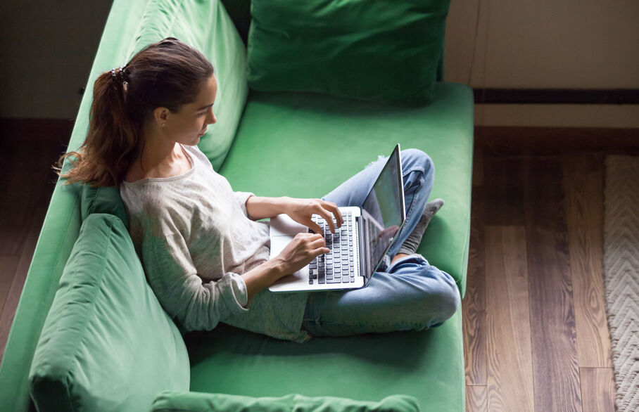 Someone sitting on a green sofa on their laptop