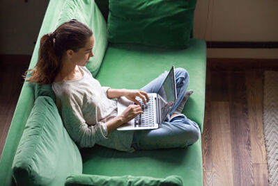 Someone sitting on a green sofa on their laptop
