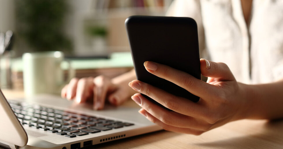Close up of woman hands using laptop checking smart phone