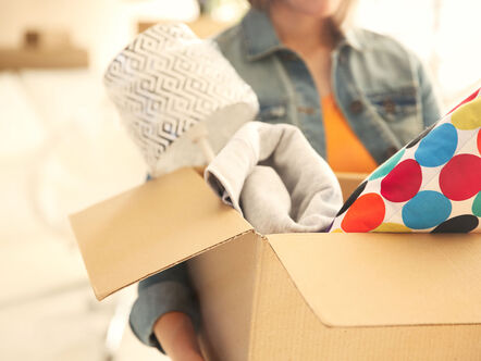 Young woman holding open cardboard box with things for moving into new house