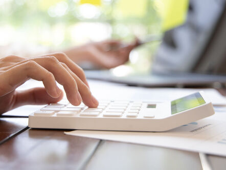 Close up of someone using a white calculator , laptop open in background 