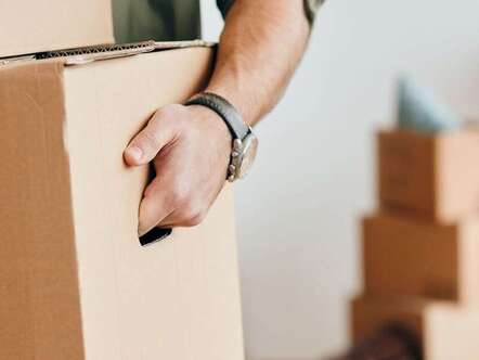 Person carrying a cardboard box with other boxes in the background